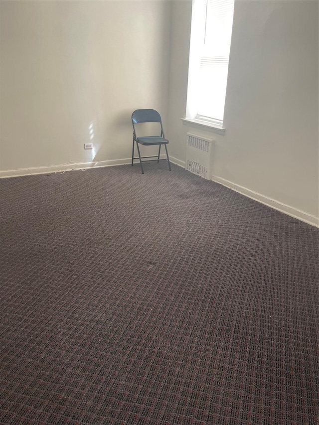 spare room featuring dark carpet, baseboards, and radiator heating unit