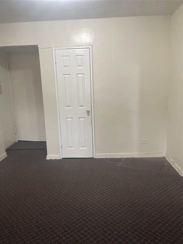 unfurnished room with dark carpet and baseboards