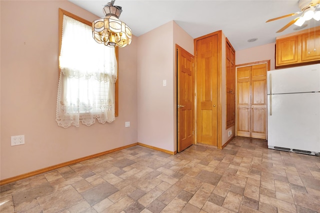 interior space with stone finish floor, ceiling fan with notable chandelier, baseboards, and freestanding refrigerator