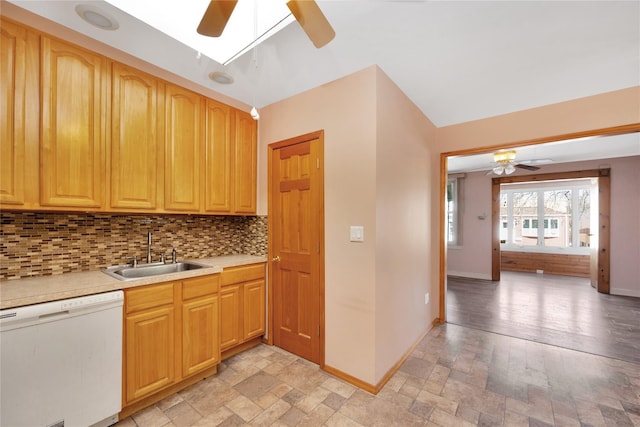 kitchen featuring backsplash, dishwasher, light countertops, stone tile floors, and a sink