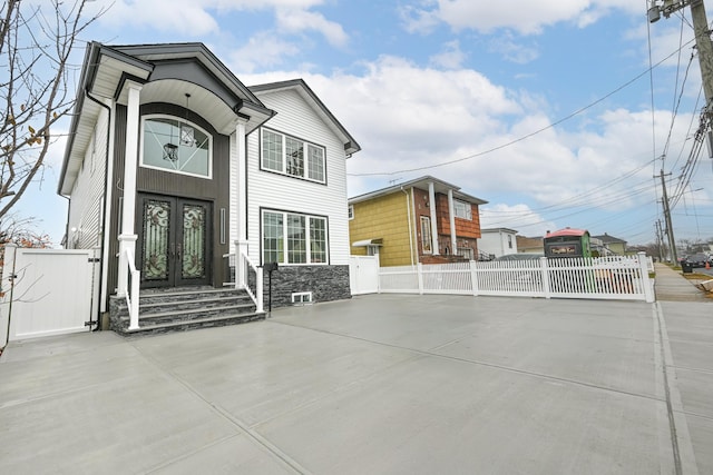 view of front of home with stone siding, french doors, fence, and a gate