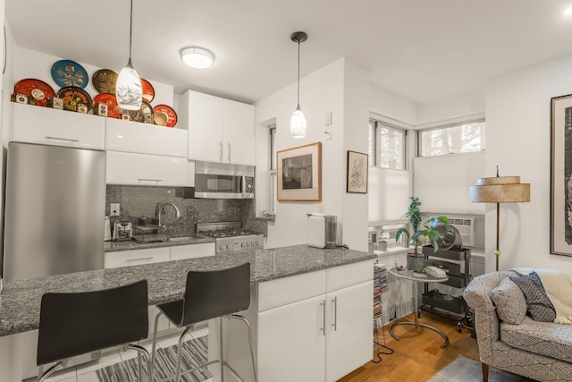 kitchen featuring light wood finished floors, backsplash, pendant lighting, appliances with stainless steel finishes, and white cabinetry