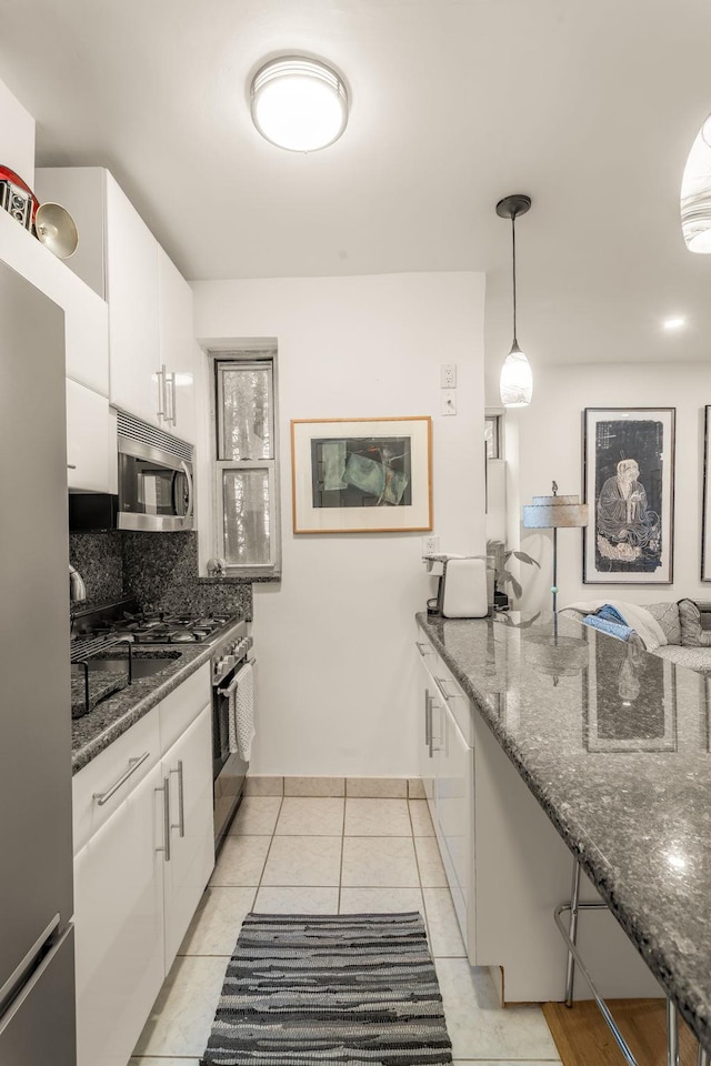 kitchen with tasteful backsplash, white cabinetry, dark stone counters, appliances with stainless steel finishes, and light tile patterned floors