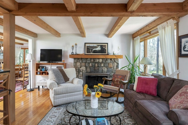 living area featuring beamed ceiling, light wood-style floors, and a stone fireplace