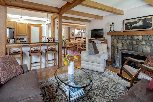 living area featuring a stone fireplace, beam ceiling, a notable chandelier, and wood finished floors