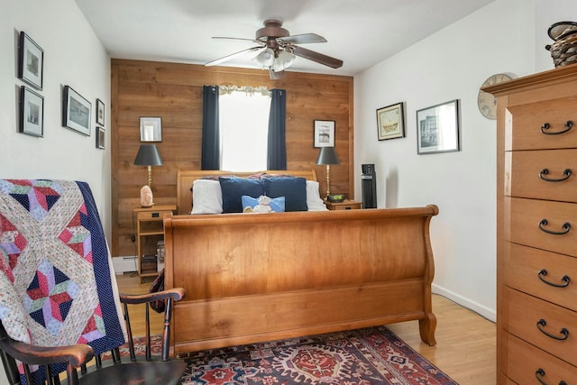 bedroom with a baseboard heating unit, wood walls, light wood finished floors, baseboards, and ceiling fan