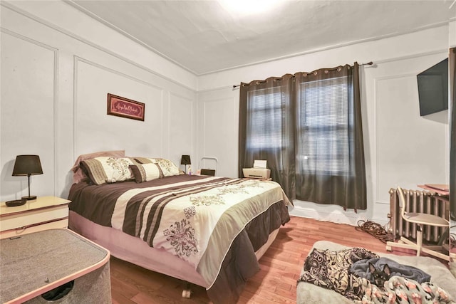 bedroom with wood finished floors, radiator heating unit, and a decorative wall