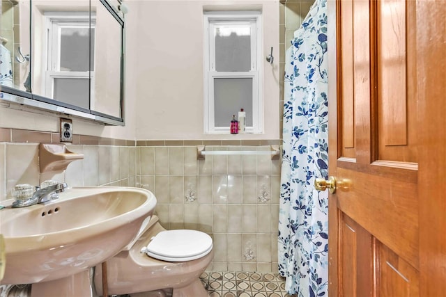 bathroom with curtained shower, tile walls, toilet, and a sink