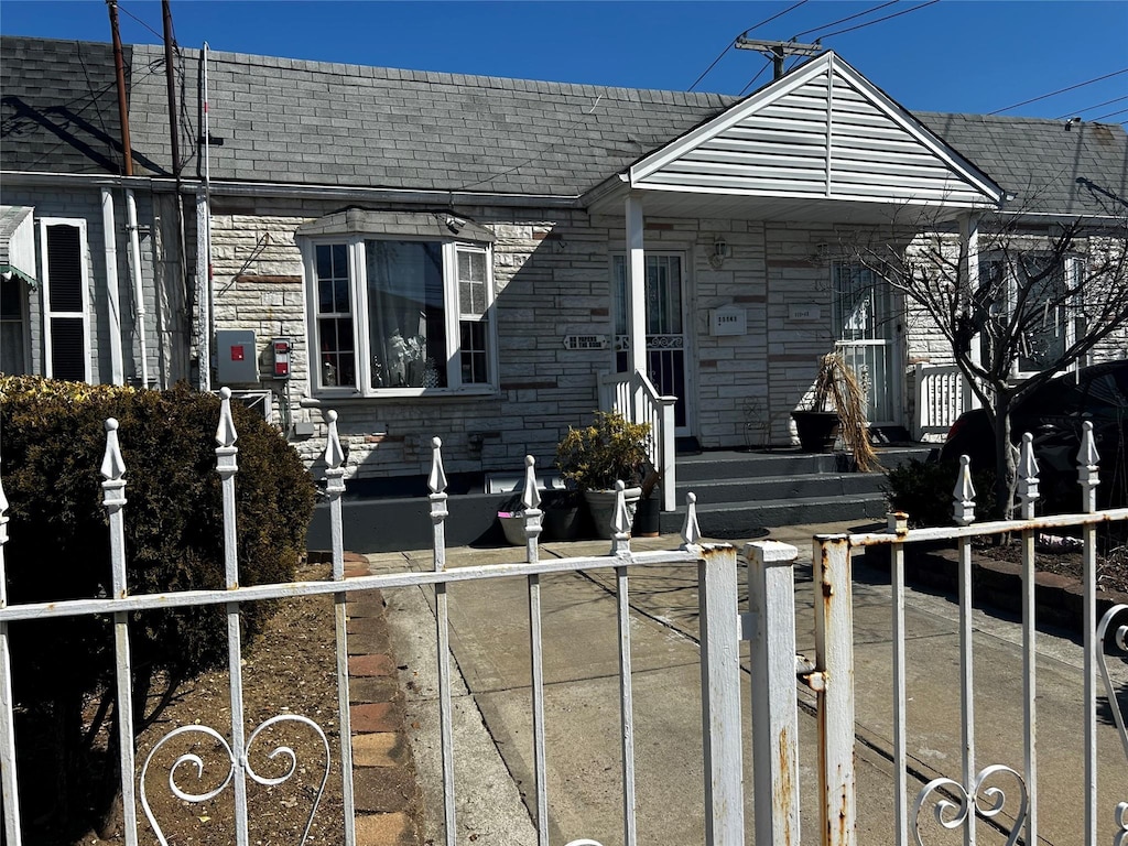 view of front of house featuring stone siding, a porch, roof with shingles, and fence