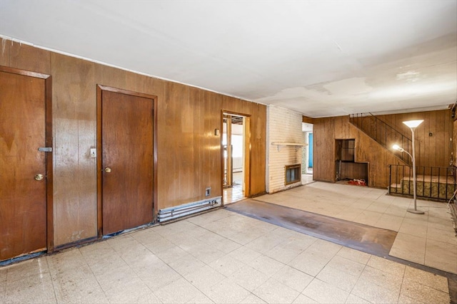 unfurnished living room featuring stairs, tile patterned floors, a brick fireplace, and wood walls