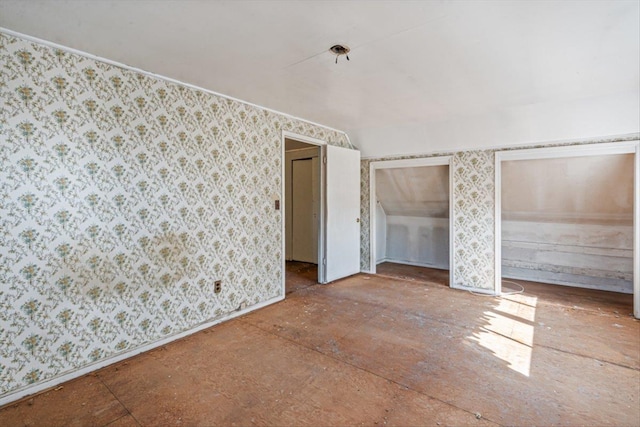 unfurnished bedroom featuring wallpapered walls, baseboards, and multiple closets