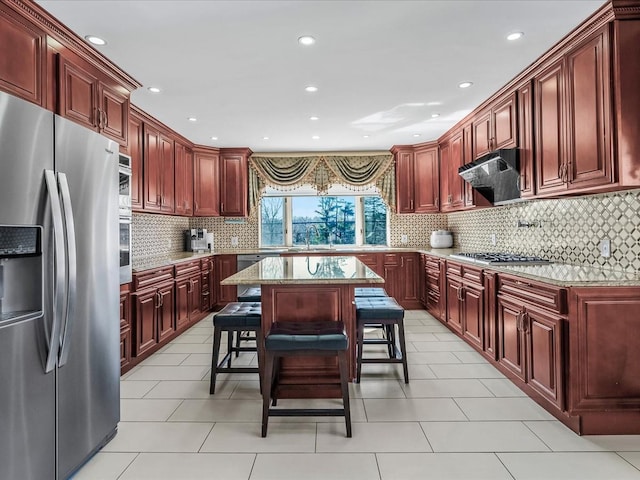 kitchen with reddish brown cabinets, light stone countertops, under cabinet range hood, appliances with stainless steel finishes, and a sink