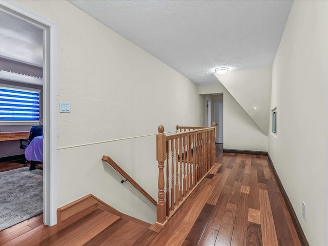 corridor with wood finished floors, an upstairs landing, baseboards, and vaulted ceiling