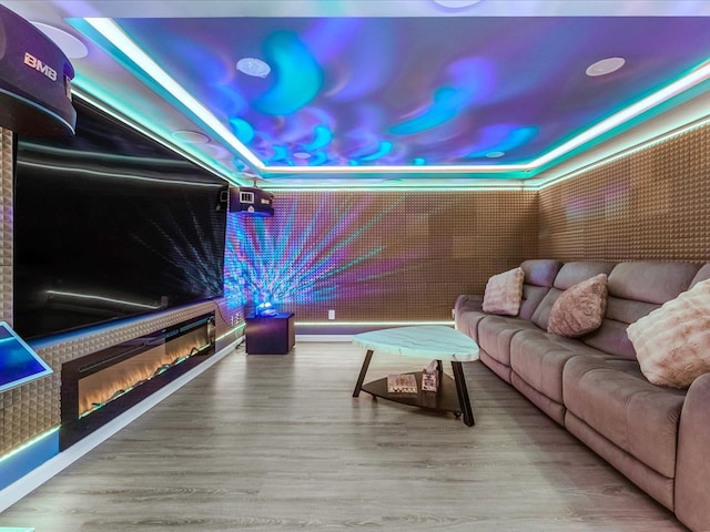 home theater room featuring a glass covered fireplace, a raised ceiling, and wood finished floors