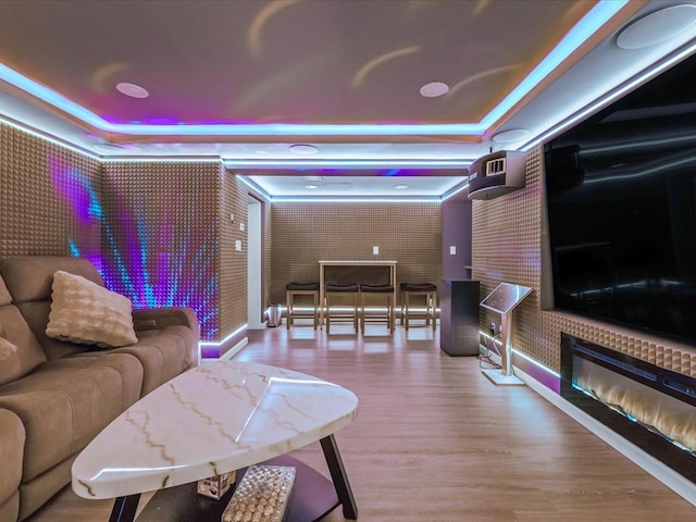 living room with a glass covered fireplace, a raised ceiling, and wood finished floors