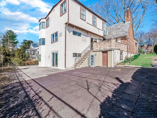 back of property featuring stairs, stucco siding, a chimney, an outbuilding, and a patio