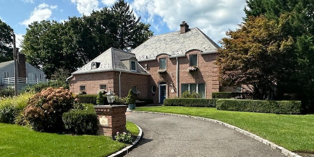 french country inspired facade with driveway, a high end roof, a front yard, brick siding, and a chimney