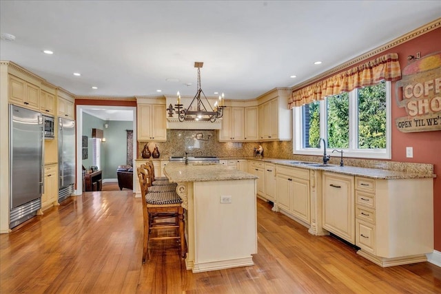 kitchen featuring a notable chandelier, built in appliances, a sink, light stone countertops, and cream cabinets