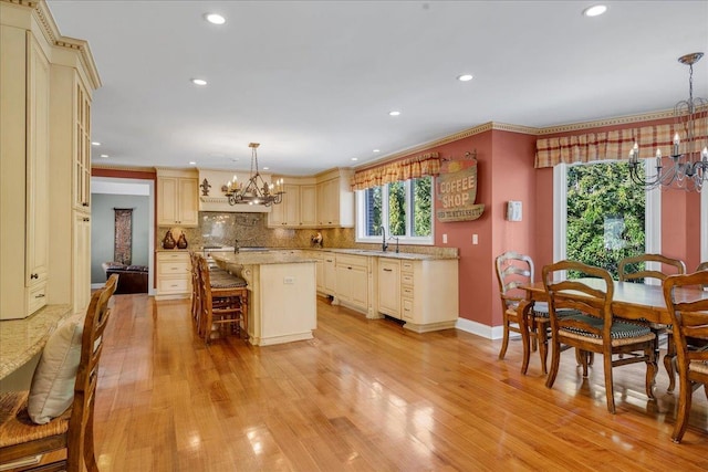 kitchen with a sink, light wood-type flooring, cream cabinets, and a chandelier