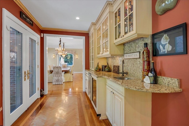 kitchen featuring glass insert cabinets, tasteful backsplash, cream cabinetry, light stone counters, and a sink
