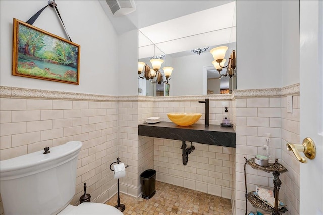 bathroom featuring toilet, an inviting chandelier, a sink, and tile walls