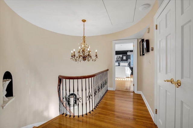corridor featuring baseboards, an upstairs landing, a chandelier, attic access, and wood finished floors