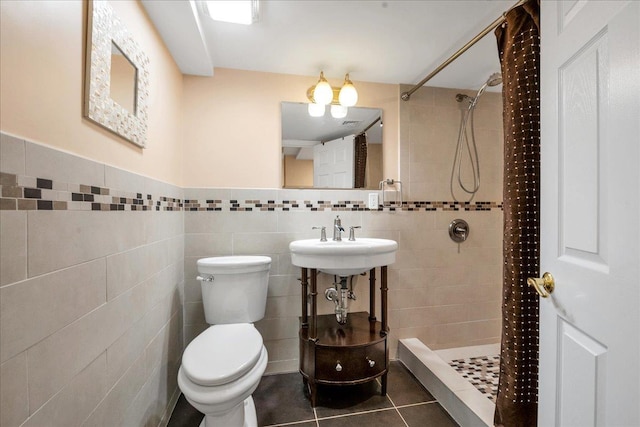 full bathroom featuring a tile shower, tile patterned flooring, toilet, a sink, and tile walls