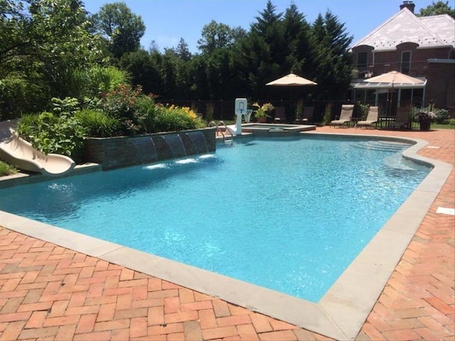 view of pool featuring a patio area, a water slide, fence, and a pool with connected hot tub