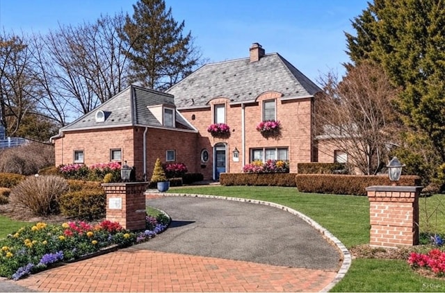 french country style house featuring a chimney, driveway, a front yard, and brick siding