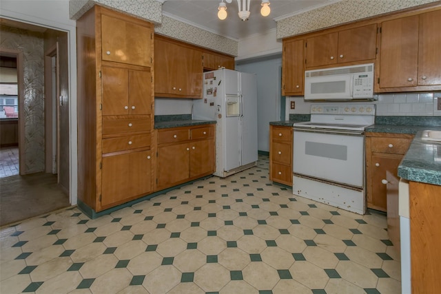 kitchen with white appliances, light floors, ornamental molding, dark countertops, and brown cabinets