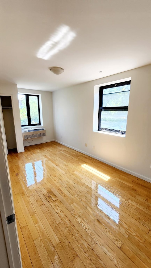 empty room featuring baseboards, light wood-style floors, and a wall mounted AC