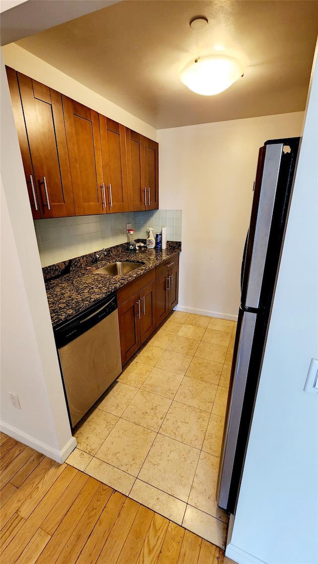 kitchen featuring freestanding refrigerator, dark stone counters, decorative backsplash, baseboards, and dishwasher