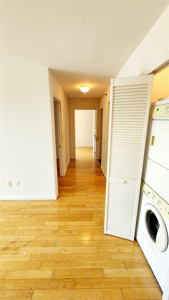 washroom featuring laundry area, light wood-style flooring, baseboards, and stacked washing maching and dryer