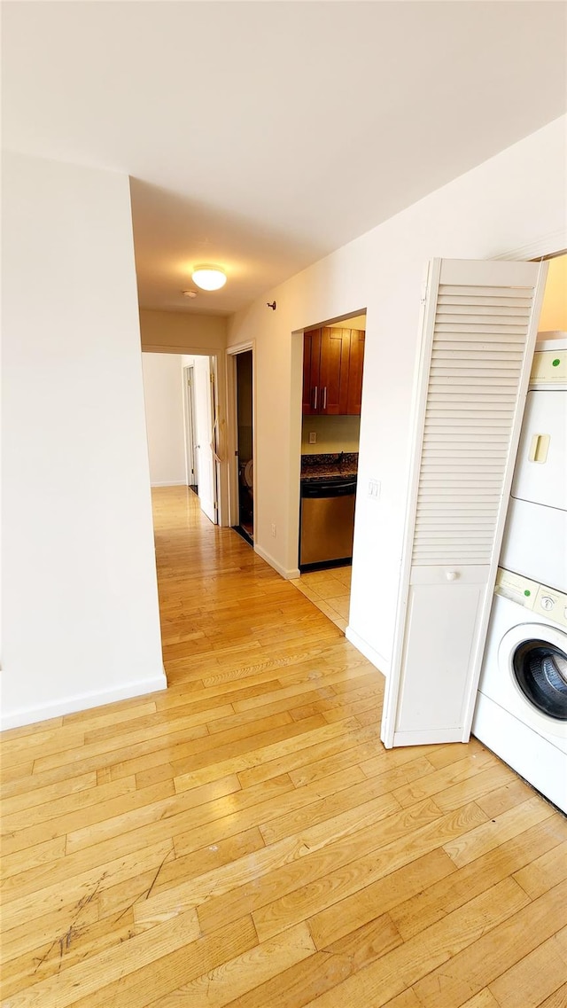 washroom featuring light wood finished floors, laundry area, stacked washer and clothes dryer, and baseboards