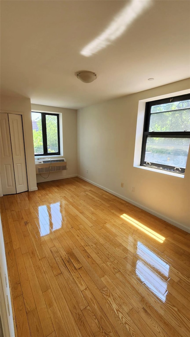 empty room featuring light wood-type flooring, baseboards, and a wall unit AC