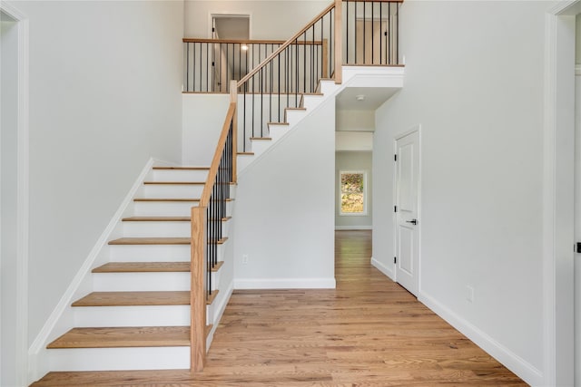 stairs with a towering ceiling, baseboards, and wood finished floors