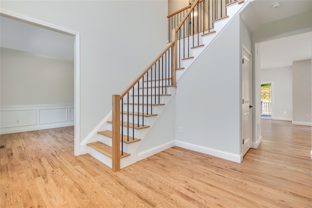 staircase featuring a decorative wall, a towering ceiling, baseboards, and wood finished floors