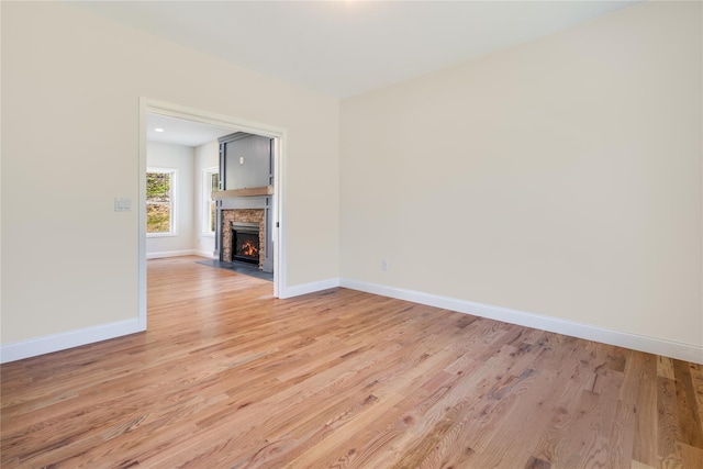 unfurnished living room with a stone fireplace, light wood-type flooring, and baseboards