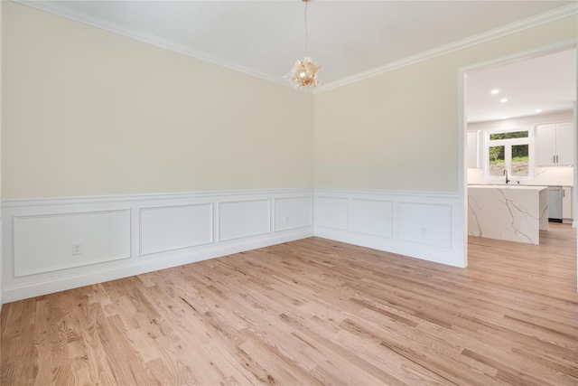 spare room with crown molding, a chandelier, light wood-style flooring, wainscoting, and a sink