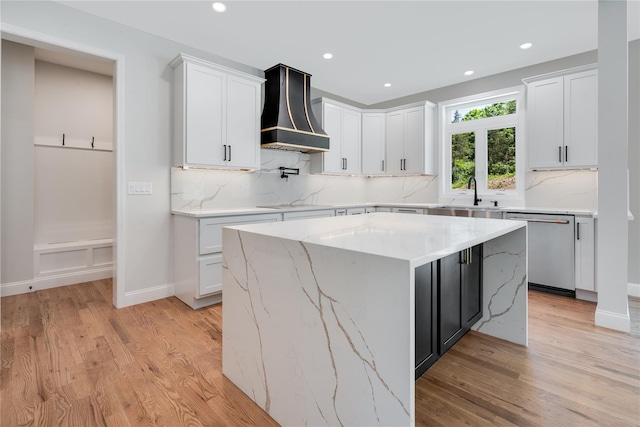 kitchen with white cabinetry, stainless steel dishwasher, custom exhaust hood, and light wood finished floors