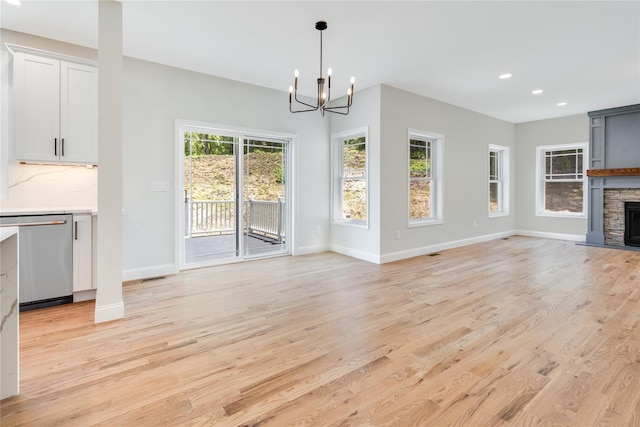 unfurnished living room with baseboards, light wood-style floors, a stone fireplace, and an inviting chandelier