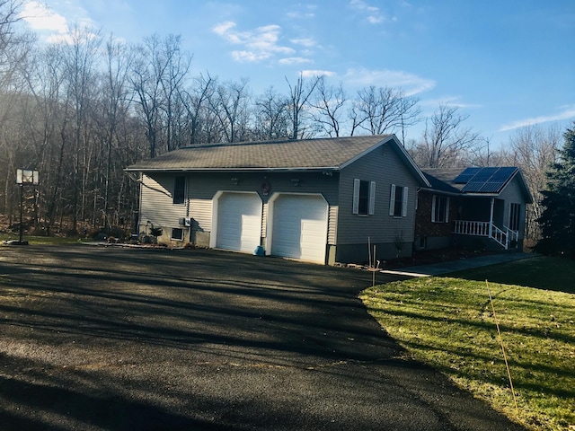 view of side of property featuring a yard, an attached garage, solar panels, and driveway