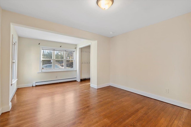 empty room with light wood finished floors, a baseboard heating unit, and baseboards