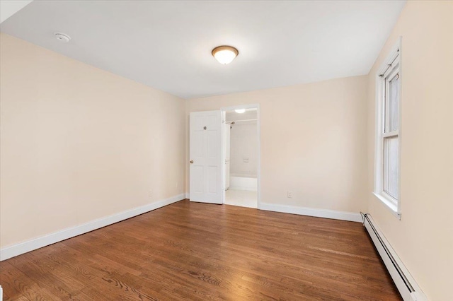 unfurnished room featuring baseboard heating, baseboards, and wood finished floors