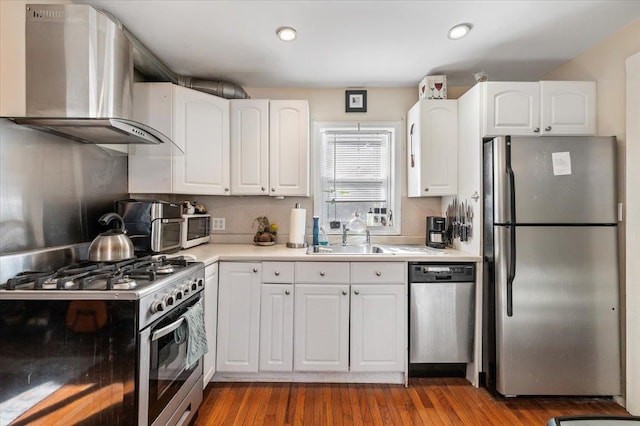 kitchen with white cabinets, appliances with stainless steel finishes, wall chimney exhaust hood, and a sink