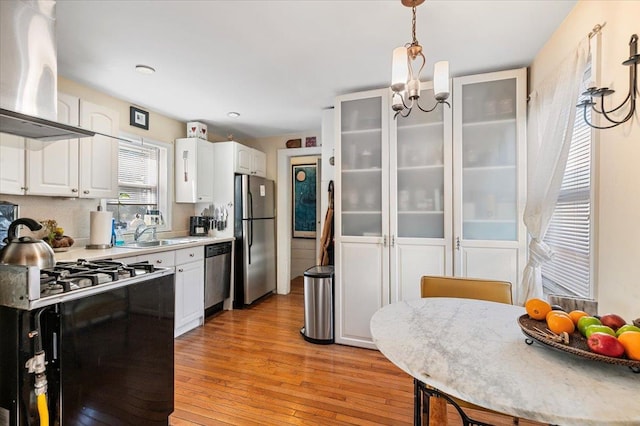 kitchen featuring light wood-style floors, island range hood, white cabinets, stainless steel appliances, and a sink