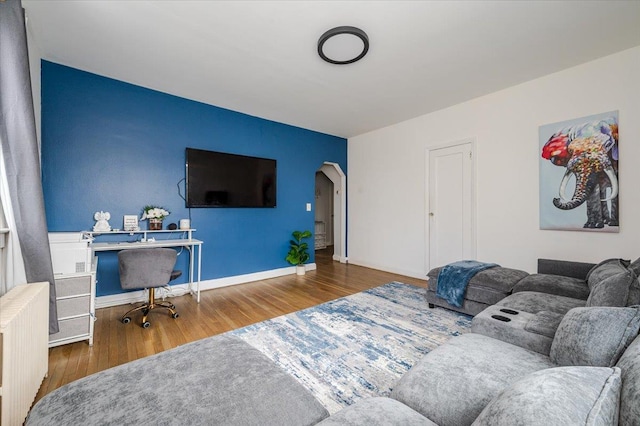 living area featuring baseboards, arched walkways, radiator, and wood finished floors