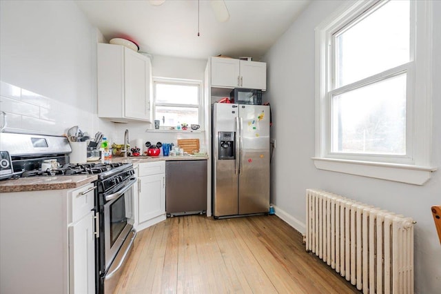 kitchen with light wood finished floors, appliances with stainless steel finishes, radiator heating unit, and white cabinetry