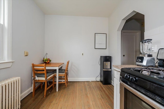 kitchen featuring light wood finished floors, radiator heating unit, stainless steel range with gas cooktop, light countertops, and baseboards