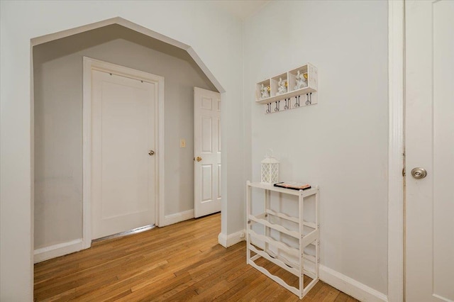 corridor with baseboards, arched walkways, and wood finished floors